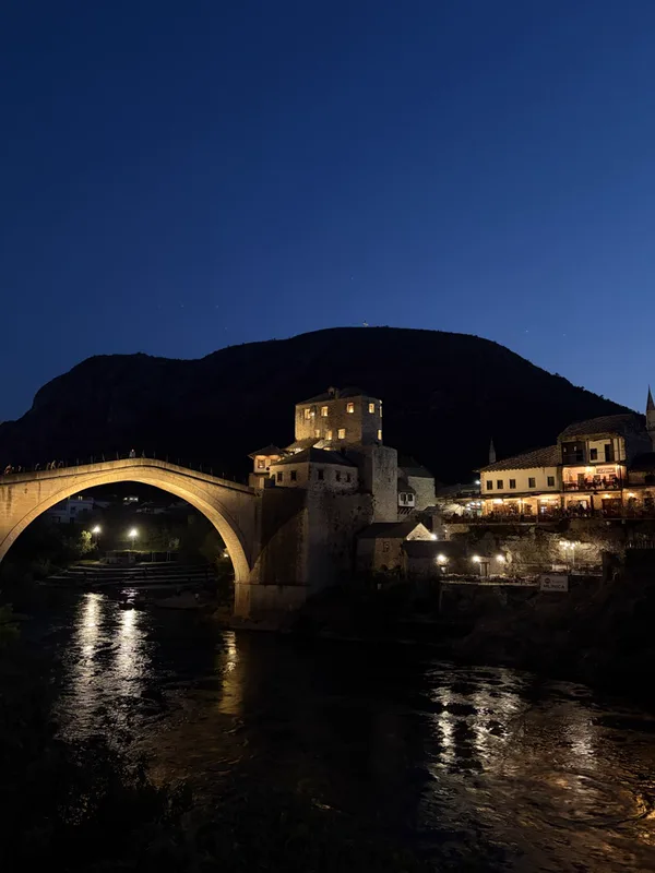 Foto de un puente de piedra en arco sobre un río, al anochecer